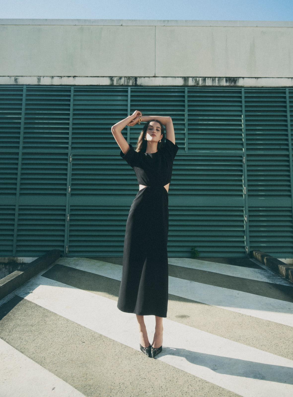Woman wearing black cutout maxi dress, black sasha mules, gold mila pearl stud earrings and satin gold elliot crystal bracelet