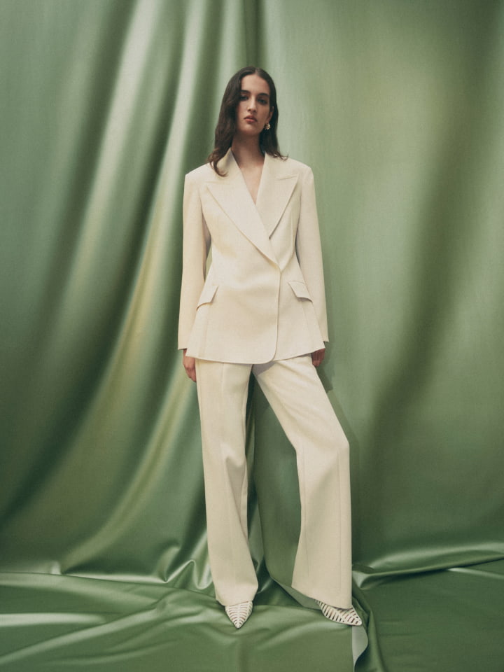 Woman wearing the stone dart blazer, stone exposed dart pant, antique white harper weave heel and gold mila pearl stud earrings