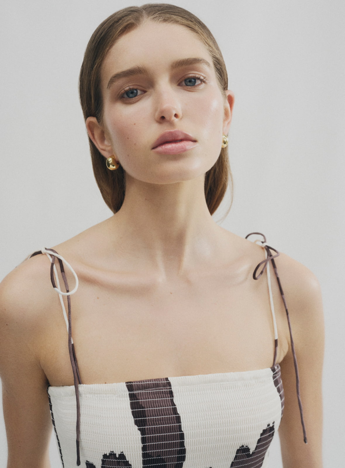 Woman in shirred print maxi dress and gold charlie huggie earrings